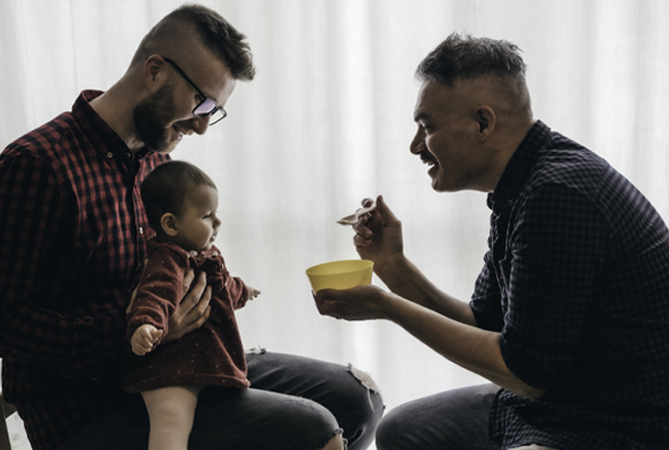 Image of two fathers feeding their baby.