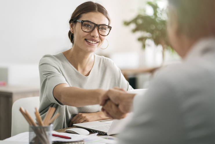 Image of a woman shaking hands with a man across her desk.