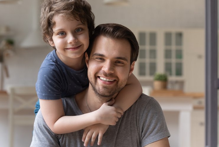 Image of son hugging father with both looking at camera.