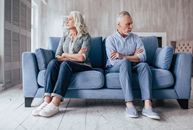 Image of older couple sitting on couch with arms crossed and backs to each other.